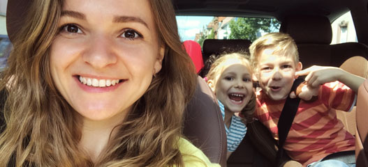 Madre en el coche con los hijos detrá haciendo muecas divertidas