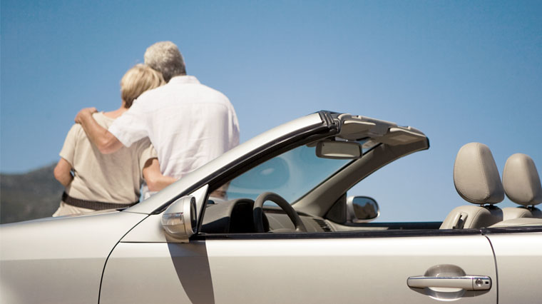 pareja mayor, de espaldas, sentados sobre el capó de un descapotable