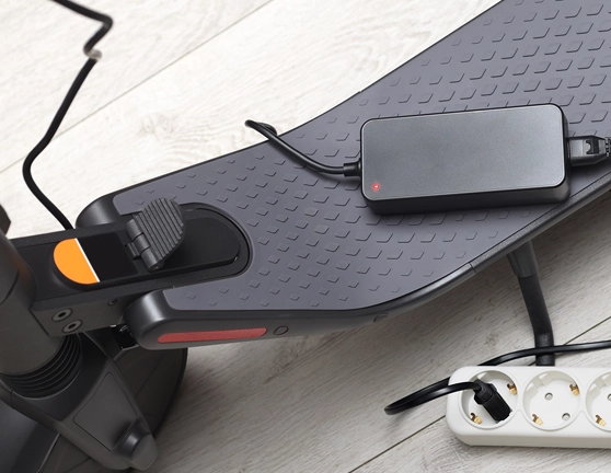 Cargador de un patinete enchufado y apoyado sobre él