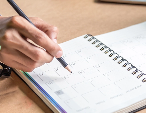 Mano derecha sosteniendo un lápiz y anotando en una agenda abierta