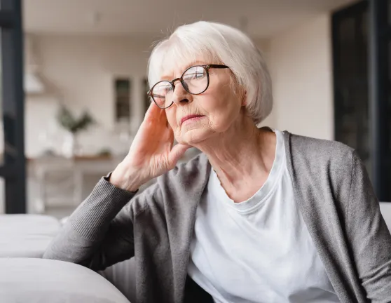 Mujer mayor pensativa, sentada en el sofá y mirando por la ventana